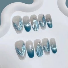 Round press-on nails with blue gradient, 3D shell and leaf decoration, and pearl accents.
