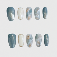 Round press-on nails with blue marble pattern, white accent nails, and gold foil decoration, combining elegance and simplicity for a refined nail look.