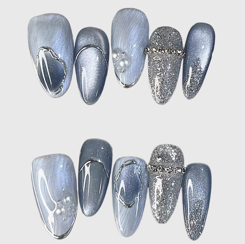 Blue oval press-on nails with cat eye effect, silver glitter, pearl and metal wave accents.