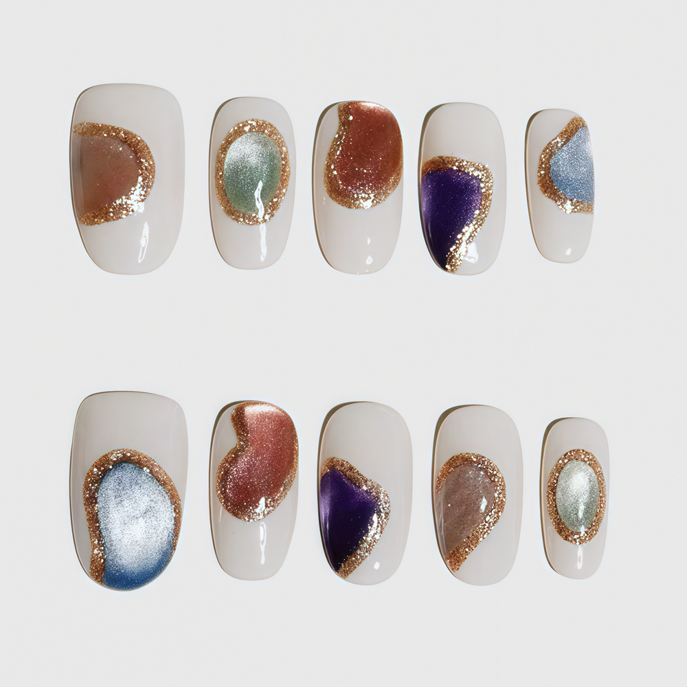 Round short press-on nails with nude base, decorated with irregular metallic color blocks outlined in gold glitter; includes blue, purple, silver, orange, and green elements in abstract style.