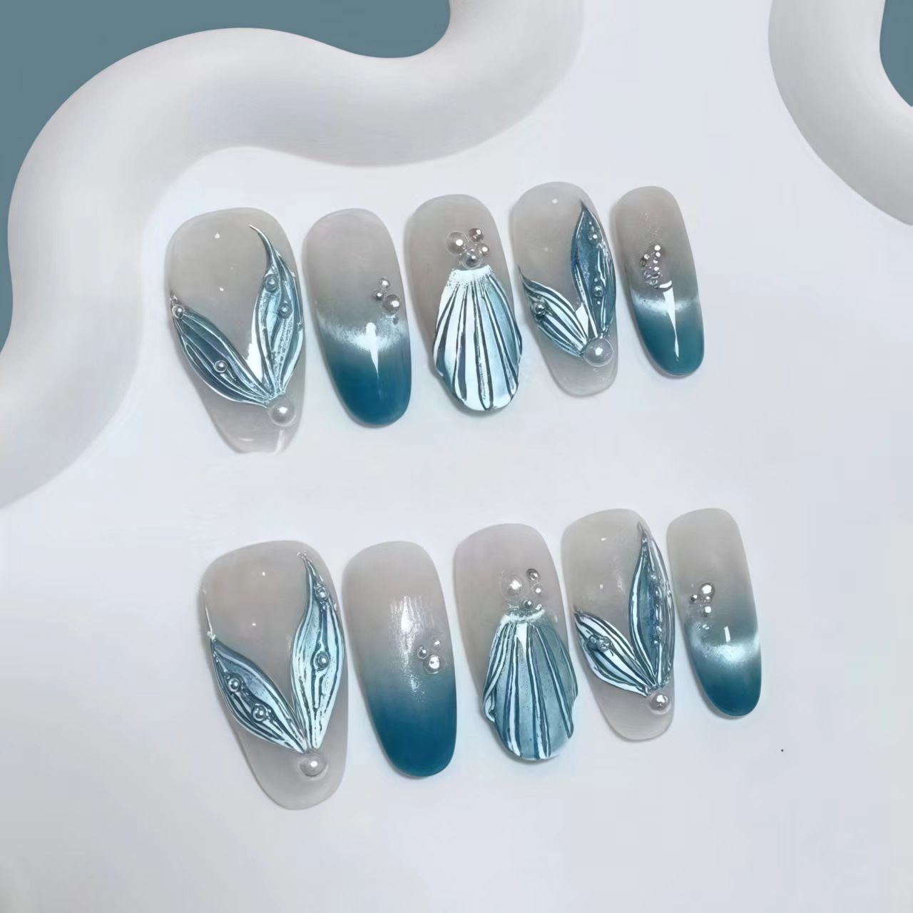 Round press-on nails with blue gradient, 3D shell and leaf decoration, and pearl accents. Main image
