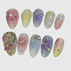 Set of oval-shaped pastel press-on nails featuring floral 3D decorations, gradient ombre colors, heart and bow motifs, and rhinestone embellishments

