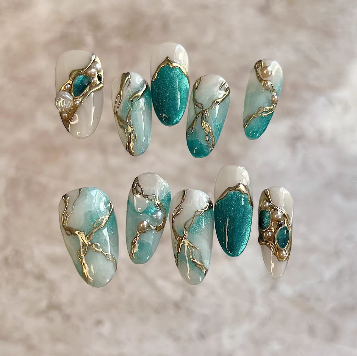 Oval-shaped green and white marble press-on nails with gold vein design and 3D pearl embellishments for a luxurious artistic look.

