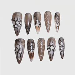 Stiletto-shaped press-on nails in metallic brown with black web lines and 3D pearl accents, gothic and futuristic reusable nail art