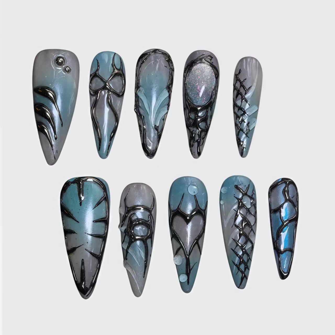 Stiletto-shaped press-on nails with bio-mechanical black detailing, chrome blue and gray gradient base, and futuristic 3D textures